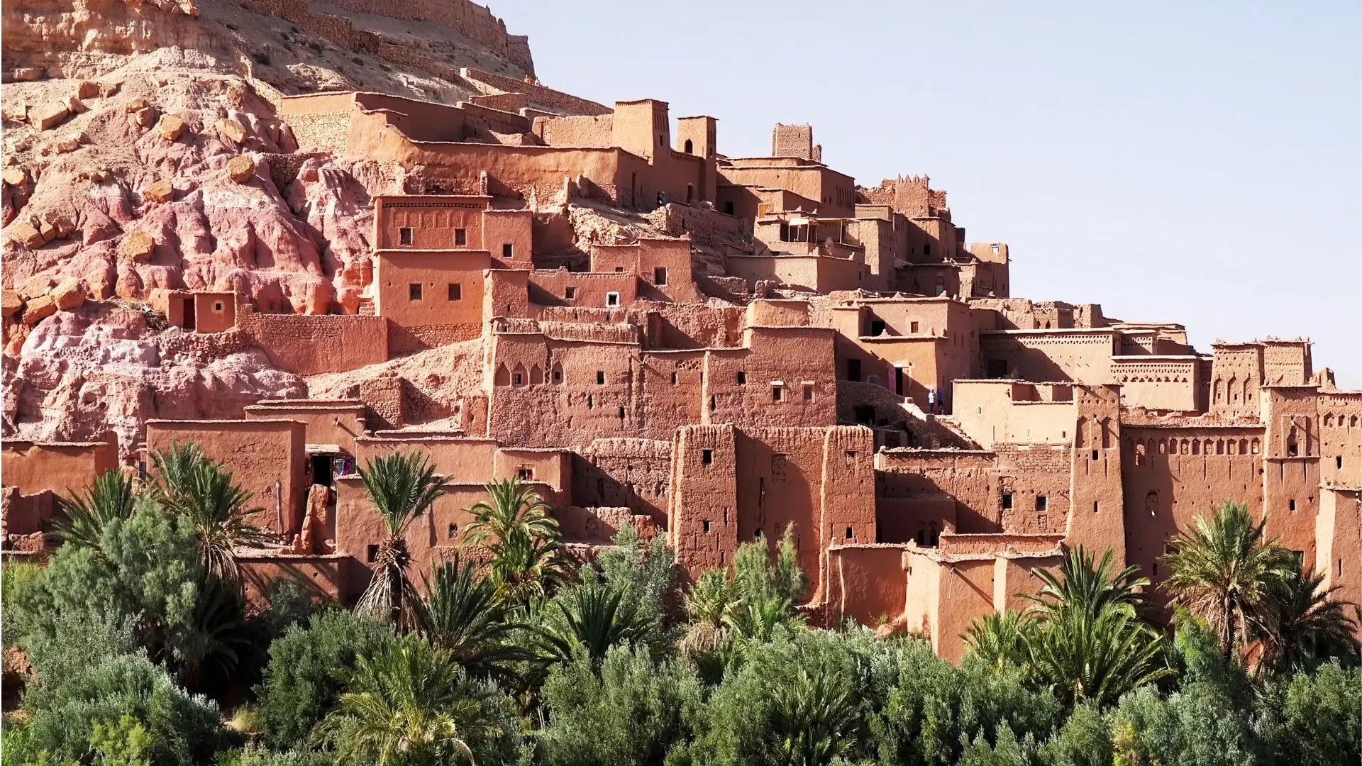 Palmiye ağaçlarının arkasında yükselen Ait Benhaddou’nun geleneksel toprak yapıları