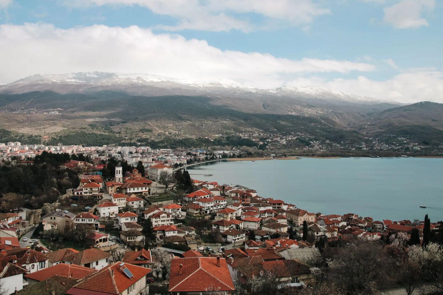 Ohrid Gölü kıyısında kırmızı çatılı evler ve gölün ardında karla kaplı dağlar
