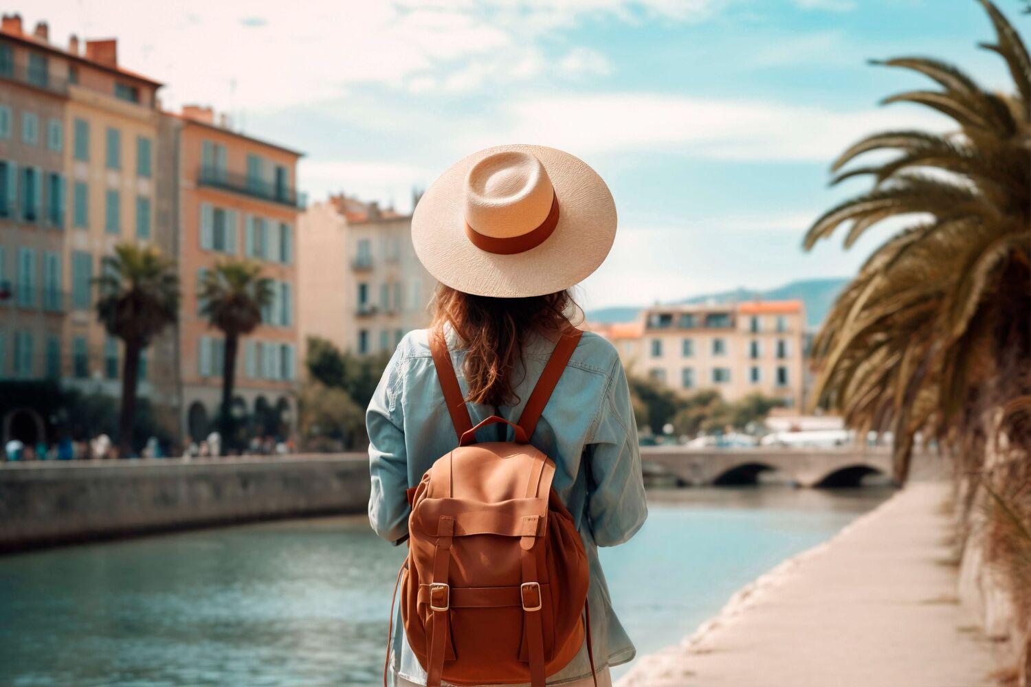 Hasır şapkalı, sırt çantalı bir kadın sahil şeridindeki renkli binalara bakıyor